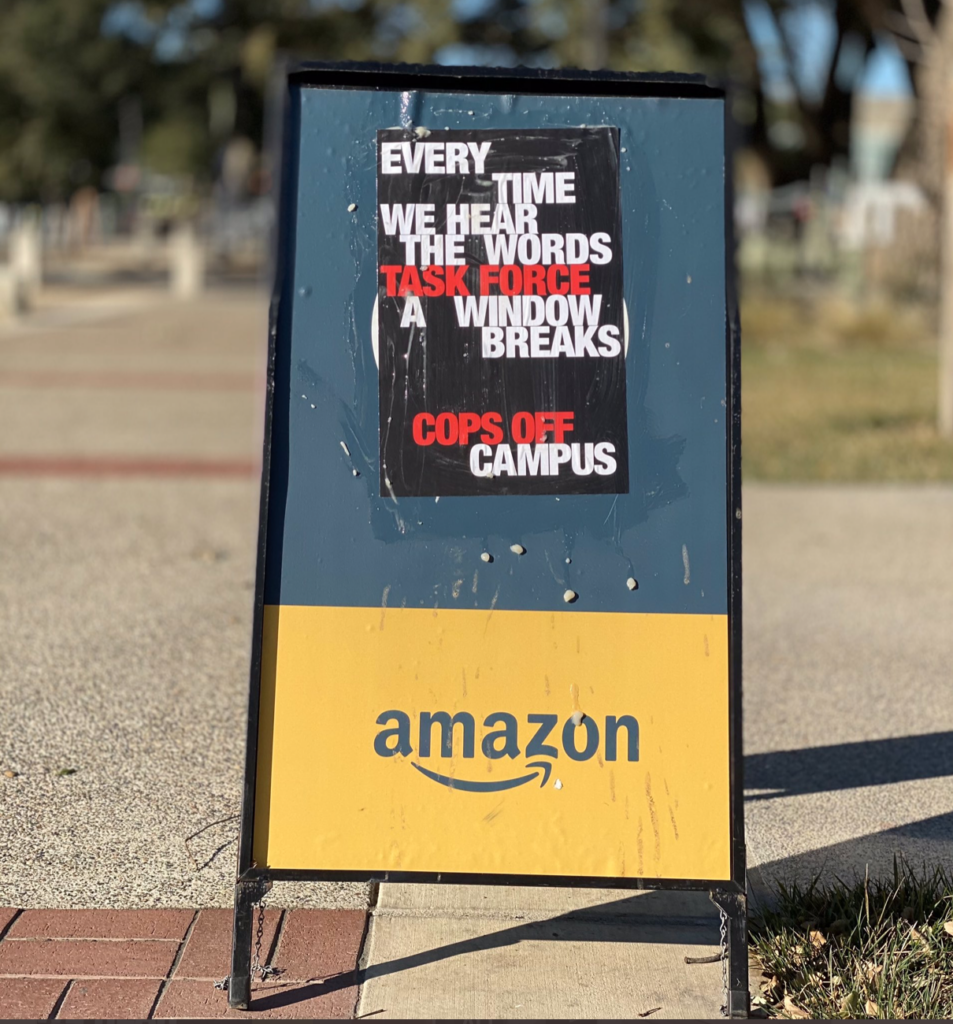 poster wheat pasted to an Amazon sign outside the campus bookstore; poster reads "every time we hear the words 'task force' a window breaks"