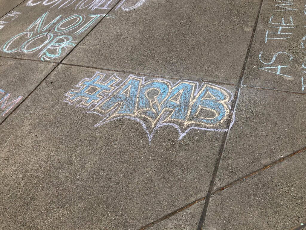 a photo of the letters ACAB written on the sidewalk in blue and yellow chalk