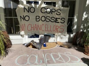 Banner reading "No Cops No Bosses No Chancellors" hung on the entrance to the Chancellor's residence; chalked word "Cowards" on the ground below