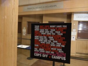 Cops Off Campus sticker on the door of Dutton Hall: Your riot cops won't save you your criminalization of dissent won't save you your tuition hikes won't save you your task forces won't save you your staff cuts won't save you your poverty wages won't save you your sad surveillance guys won't save you your fake office of diversity equity and inclusion won't save you more pepper spray definitely won't save you we could save you but we're not going to. cops off campus