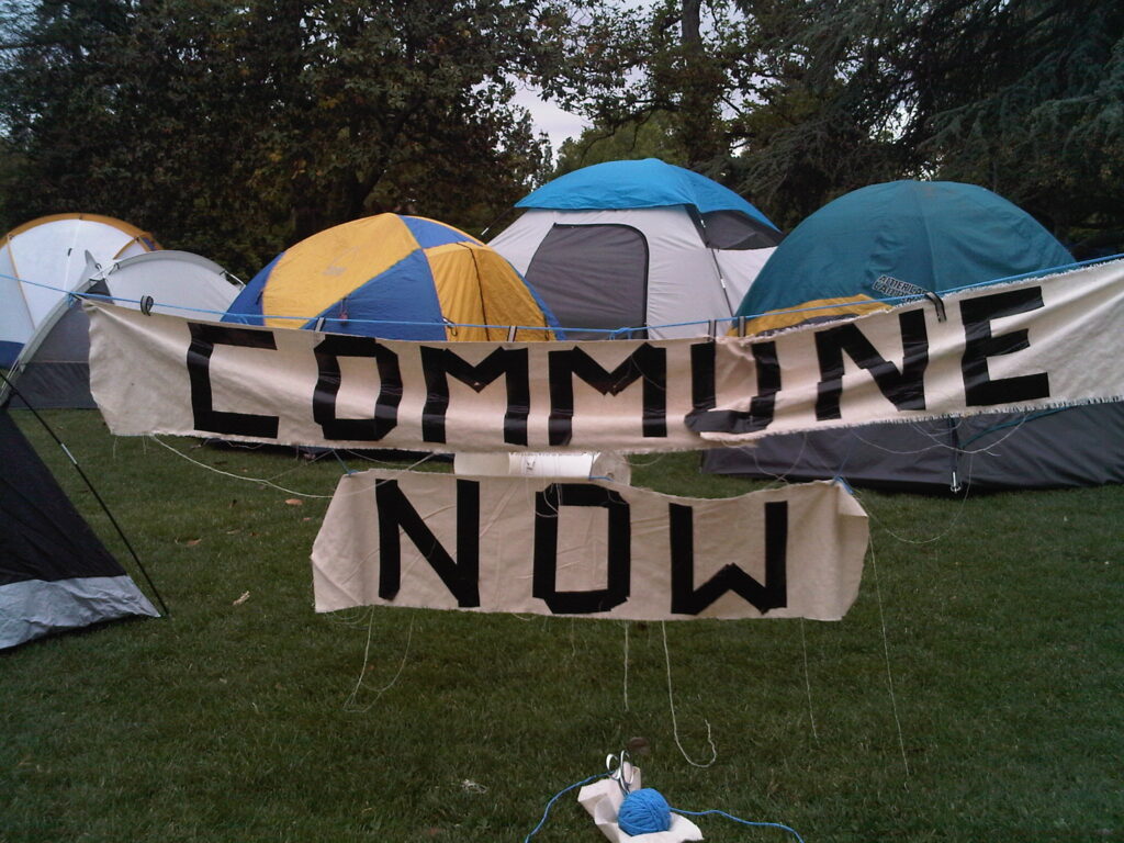 Commune Now sign in front of blue and yellow tents
