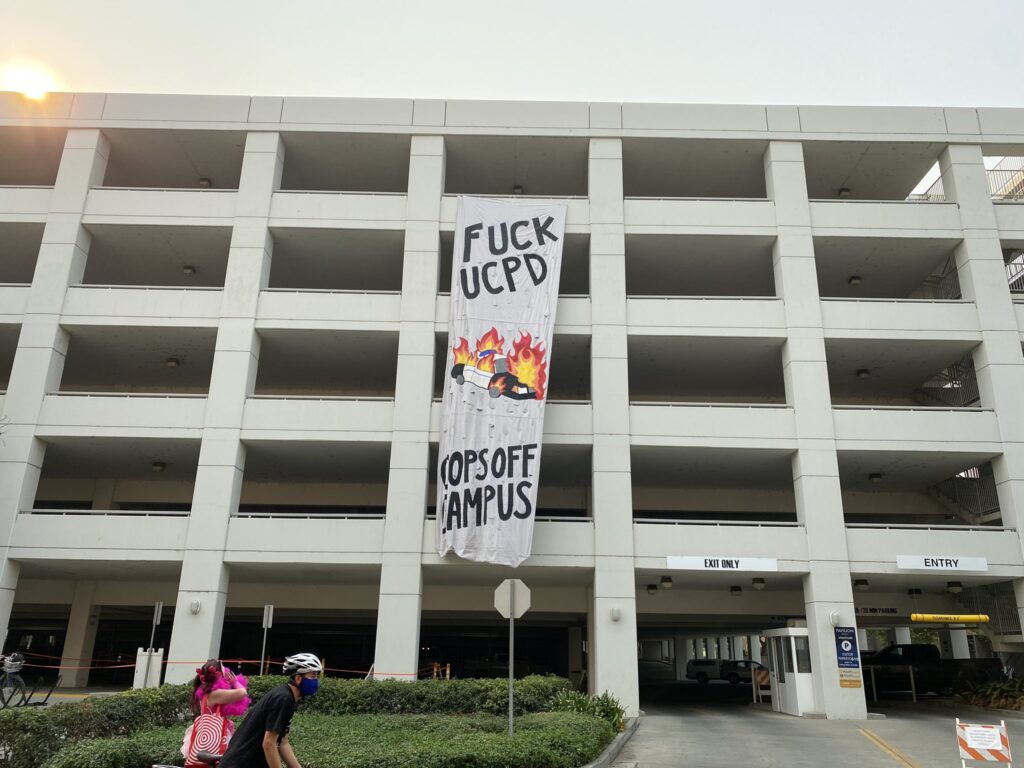 banner drop from UC Davis parking garage next to police station: banner reads "Fuck UCPD, Cops Off Campus" with image of burning police car