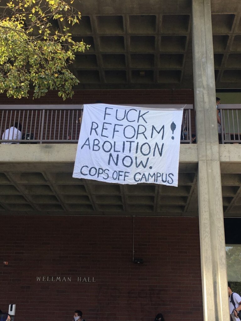 Banner drop at Wellman Hall reading "Fuck reform; abolition now; cops off campus"