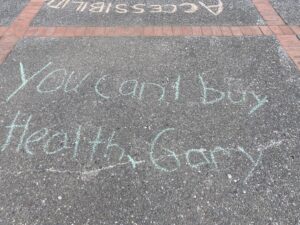 chalking on the ground in front of Mark Hall reading "You can't buy health, Gary"