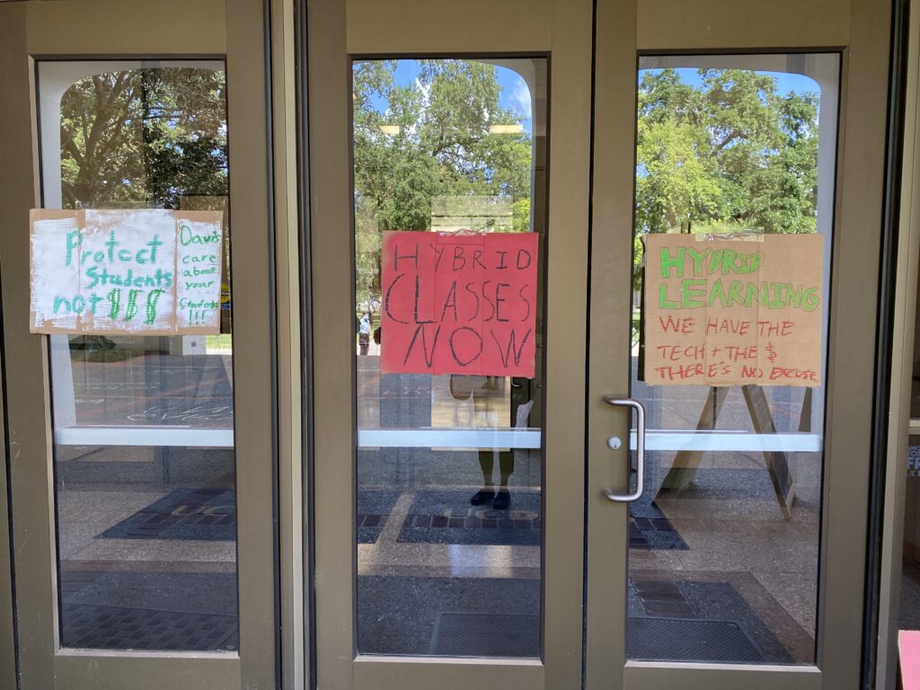 Signs reading "Protect students not $$$"; "Hybrid classes now" on the doors of Mrak Hall
